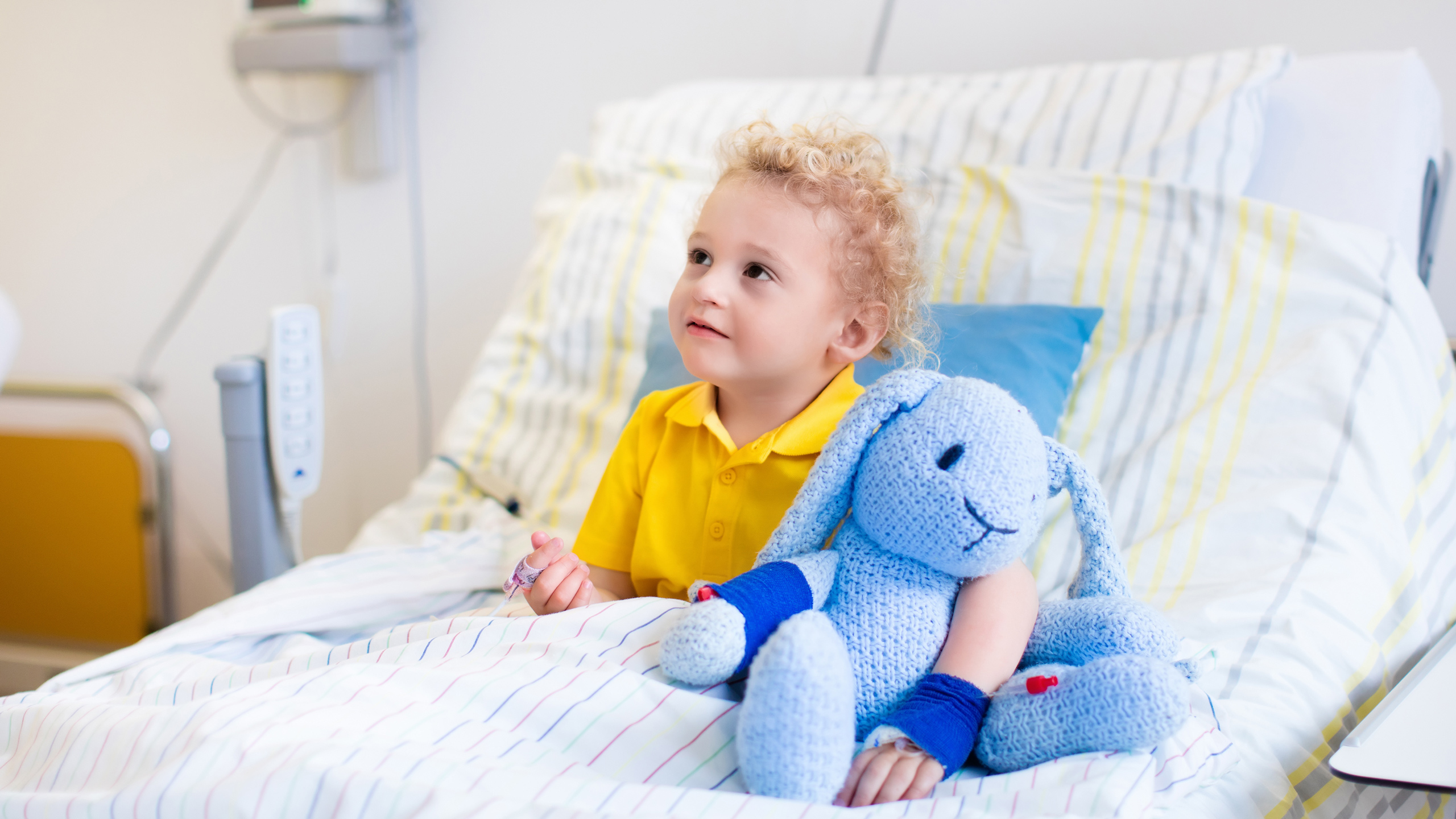 Kind in einem Krankenbett mit einem Plüschtier im Arm